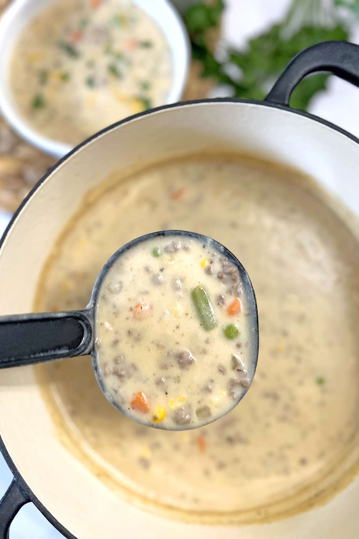 A close-up of a ladle filled with creamy Shepherd’s Pie Soup, featuring ground beef, colorful vegetables, and a thick, savory broth, served in a white Dutch oven.