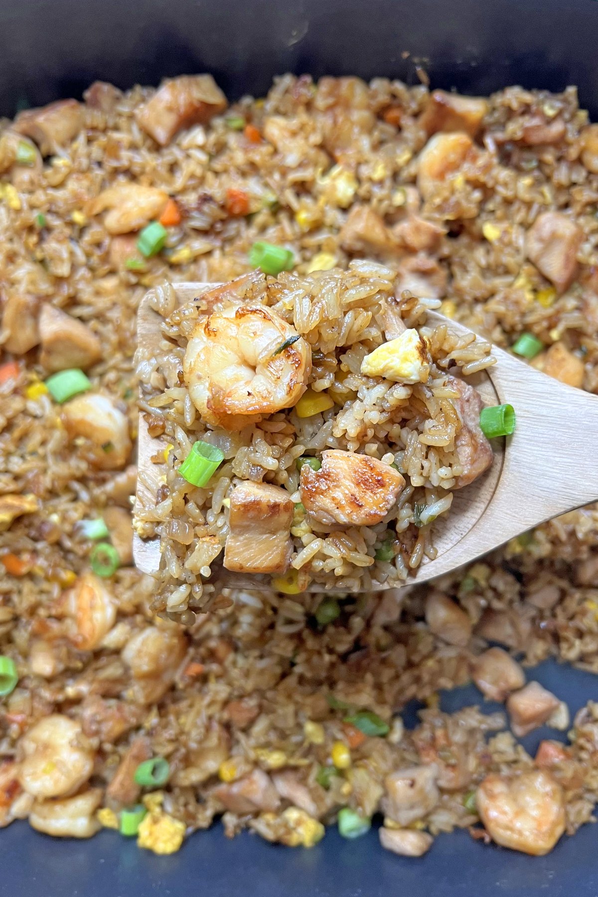 shrimp and chicken fried rice in skillet with a wooden spoon
