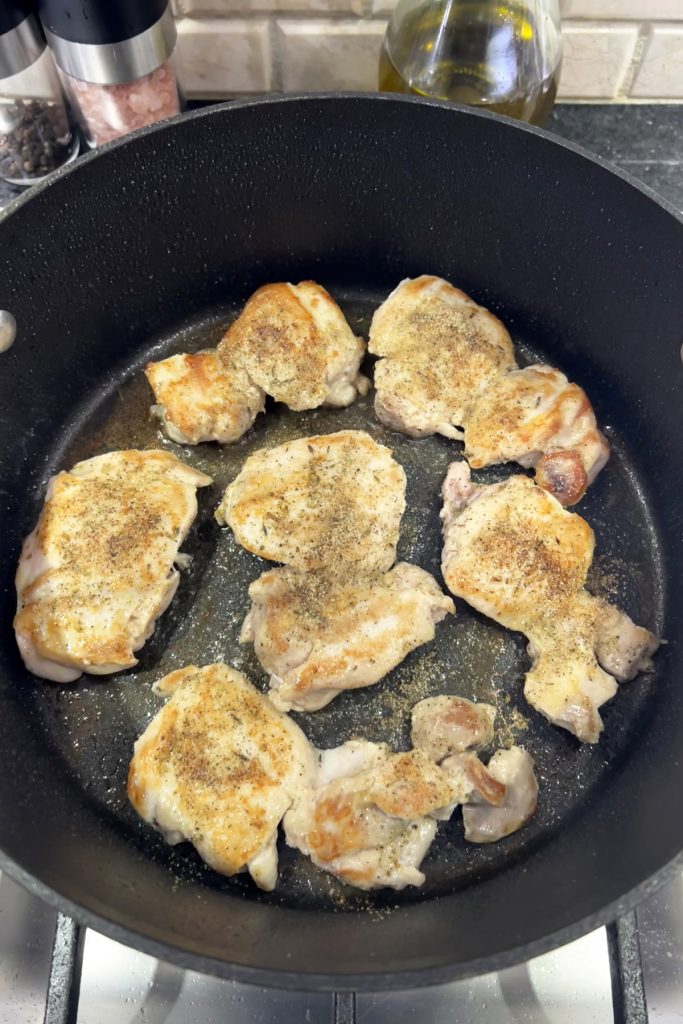 Chicken thighs cooking in a skillet.