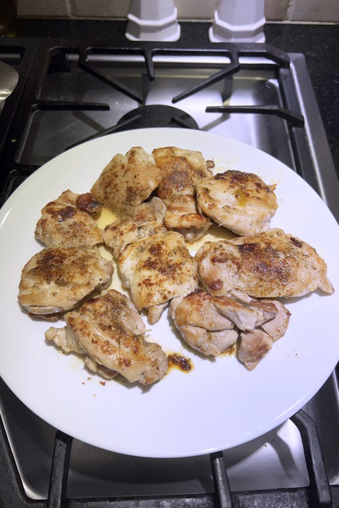 Browned chicken thighs sitting on a white plate.