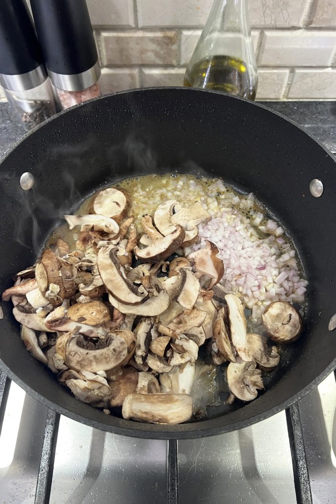 Sliced mushrooms and chopped shallots in a pan.