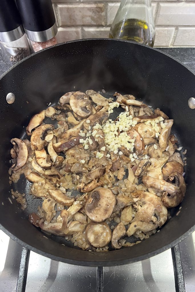 Sliced mushrooms, shallots, and minced garlic cooking in a skillet.