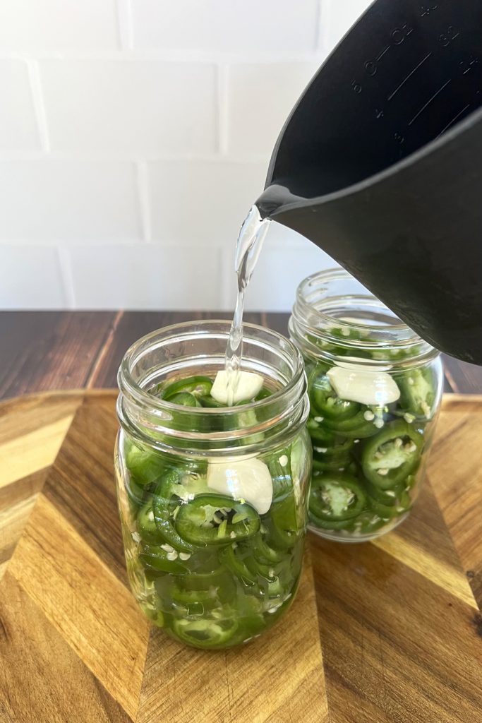 Brine being poured in a glass jar with sliced jalapeno peppers
