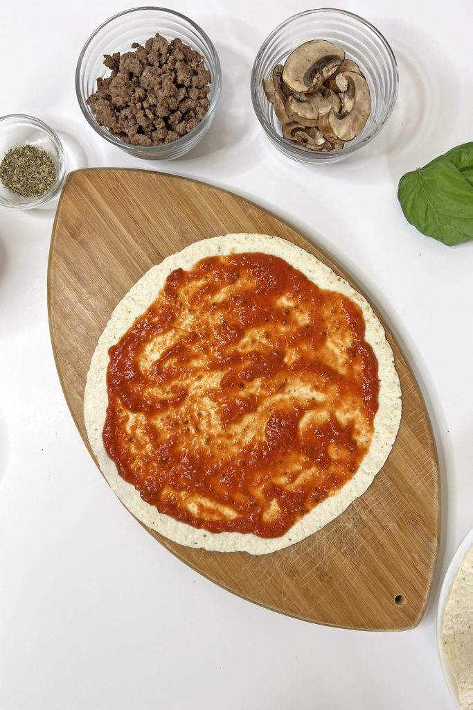 Place tortilla on a cutting board and add pizza sauce.