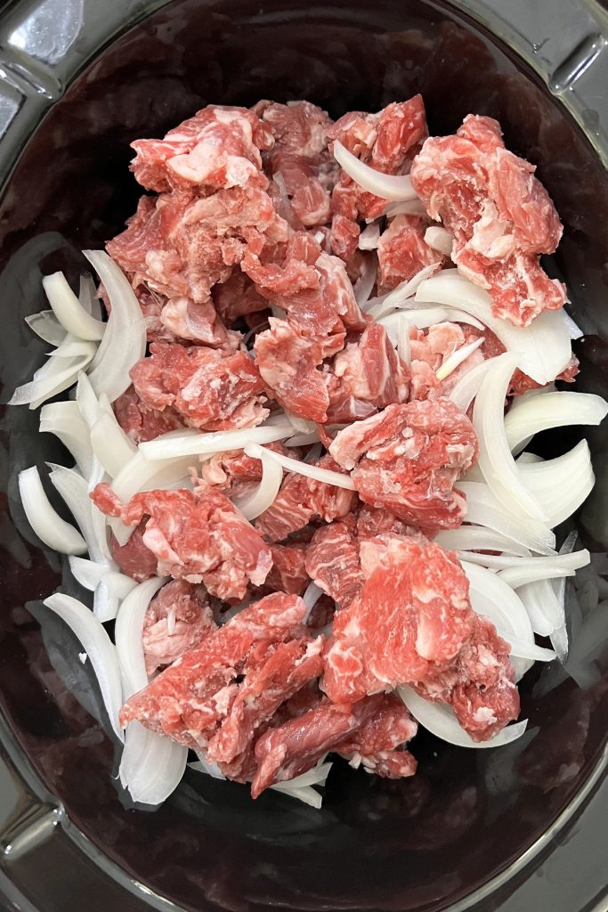 Stew meat and onions in a crockpot.