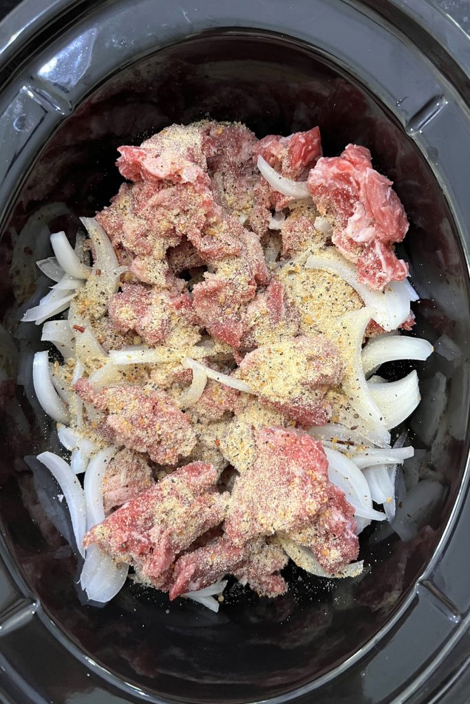 Stew meat, onions, and seasonings in a crockpot.