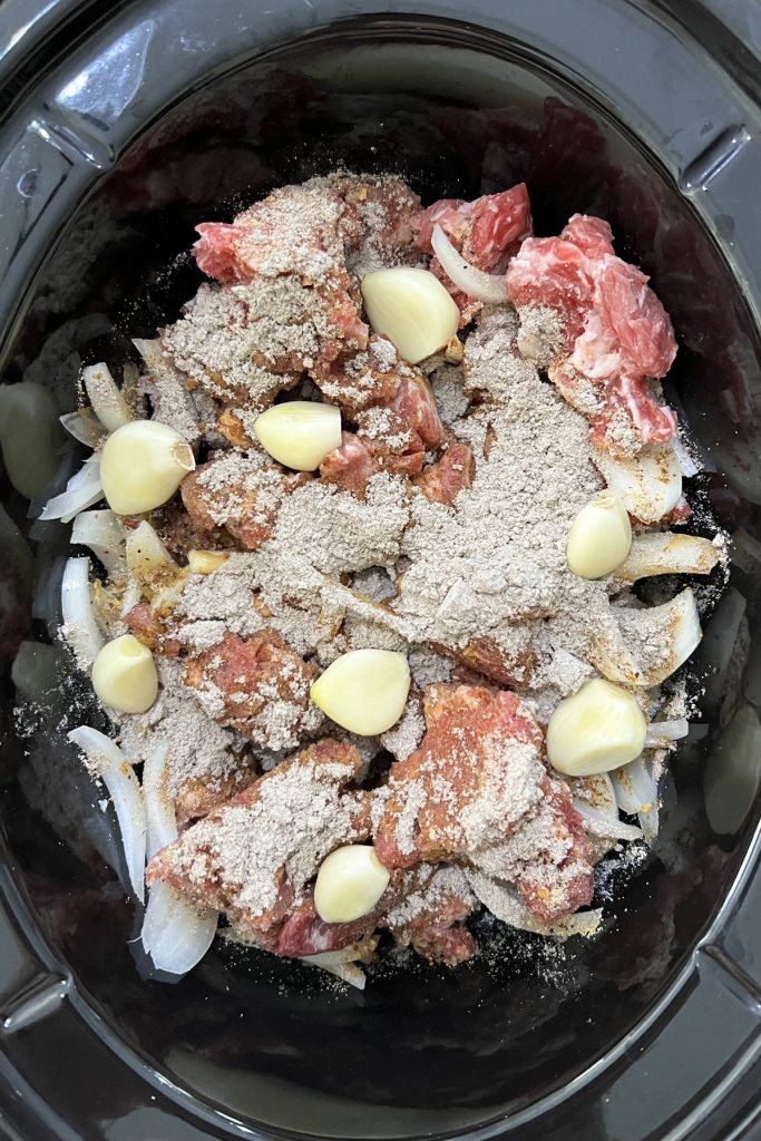 Seasoned stew meat, onions, and garlic in a crockpot.