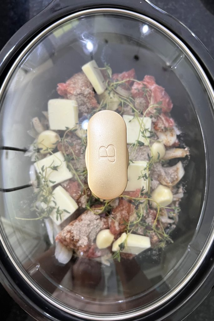 Stew meat in a crockpot with seasonings, garlic, and butter with the lid on.