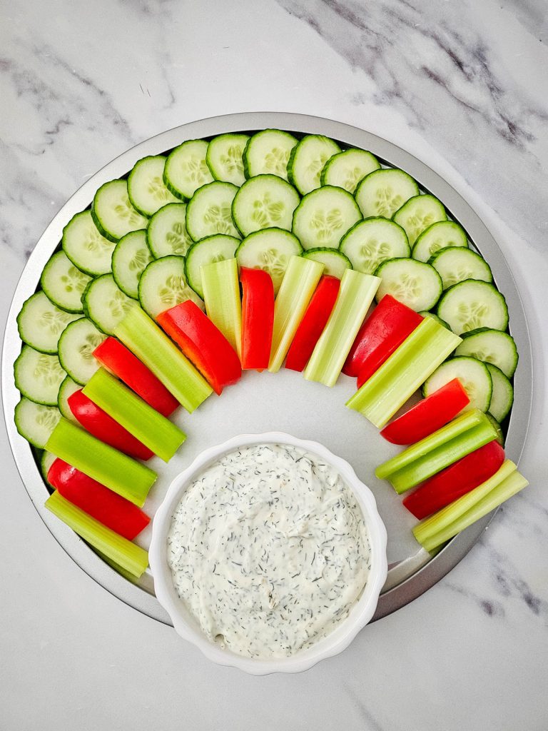sliced vegetables on a tray with a bowl of dip