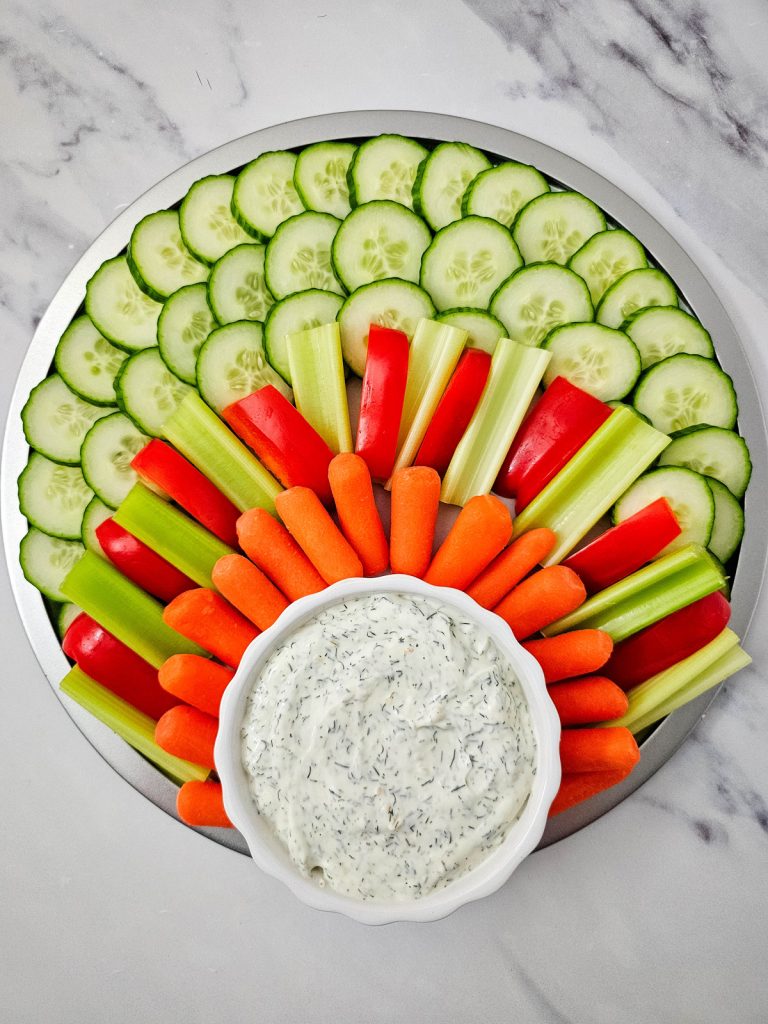 sliced vegetables on a tray with a bowl of dip