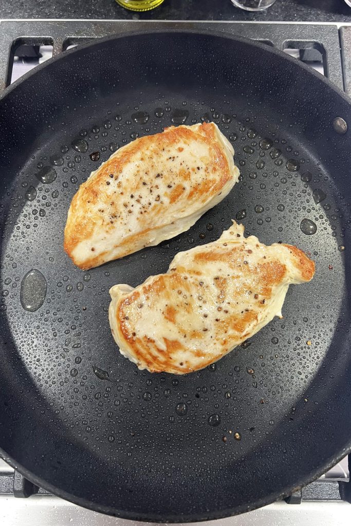 two chicken breasts cooking in a skillet