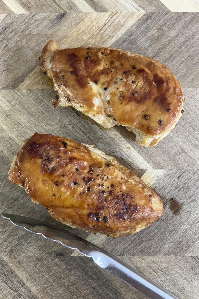 two cooked chicken breasts laying on a cutting board