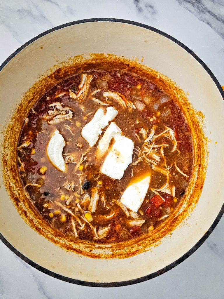 Cream cheese being added to soup in a pot.