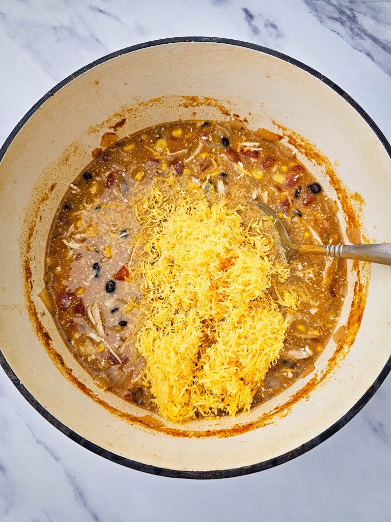 Shredded cheese being added to soup in a pot.
