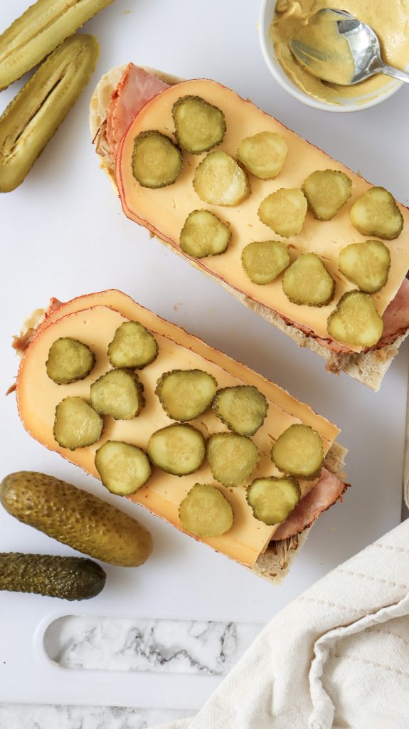 An open faced cuban sandwich with sliced pickles on top of sliced swiss cheese.