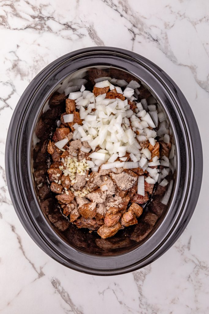 Seared beef, onions, garlic, and seasonings in a crockpot.