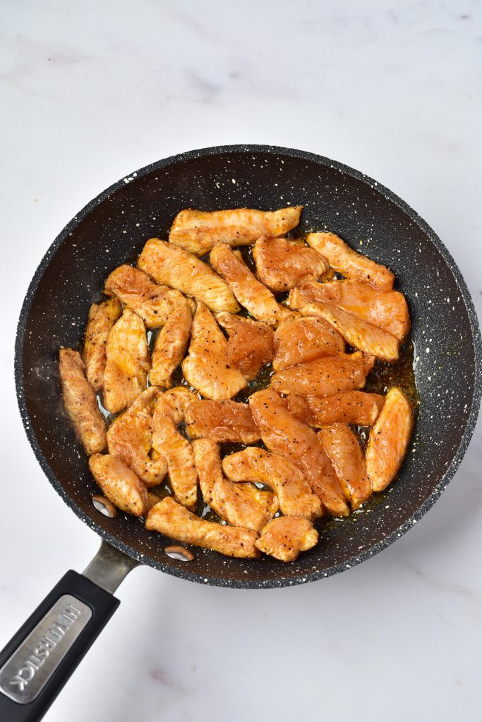 Chicken strips cooking in a skillet.
