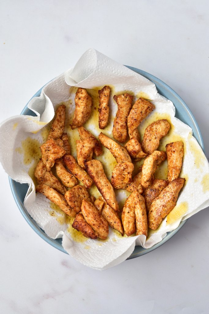 Chicken strips resting on a paper-towel lined plate.