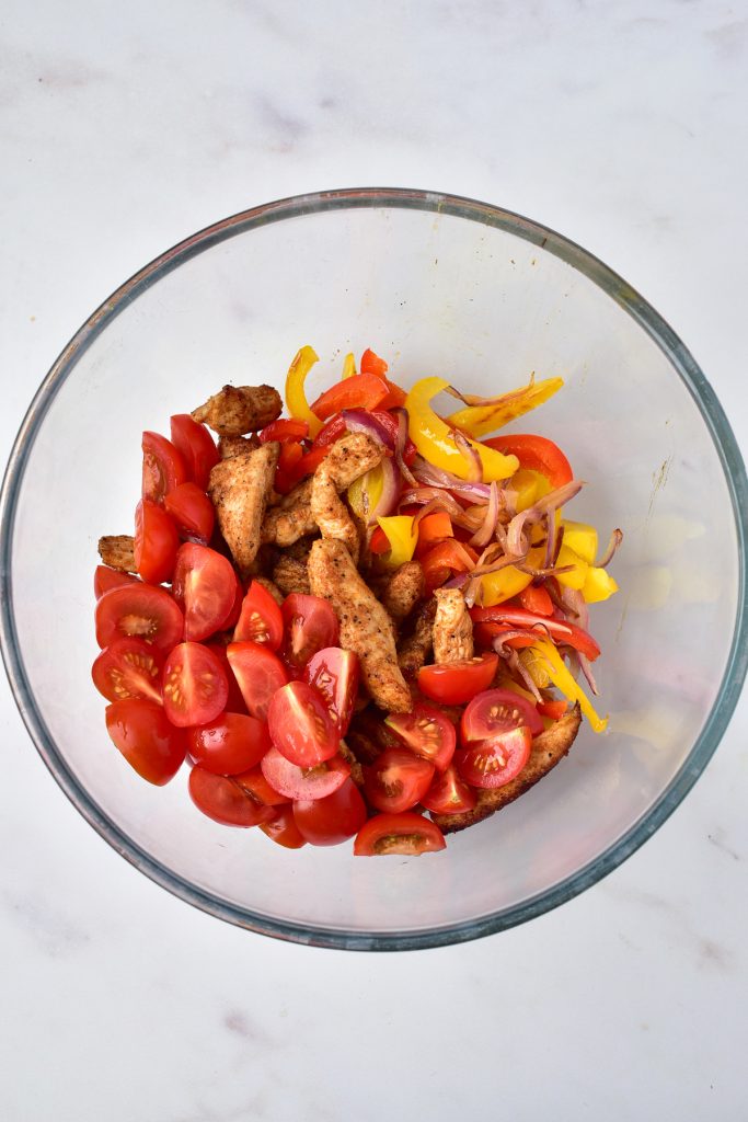 Chicken, bell peppers, onions, and tomatoes in a bowl.