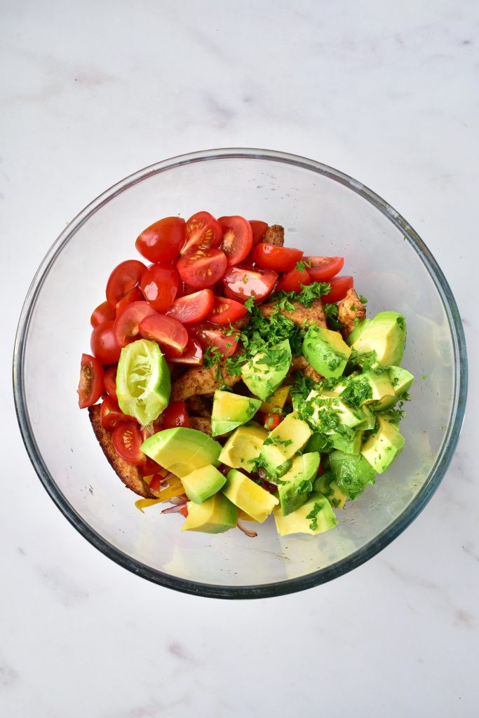 A chicken bowl with tomatoes, avocado, cilantro, and bell peppers.
