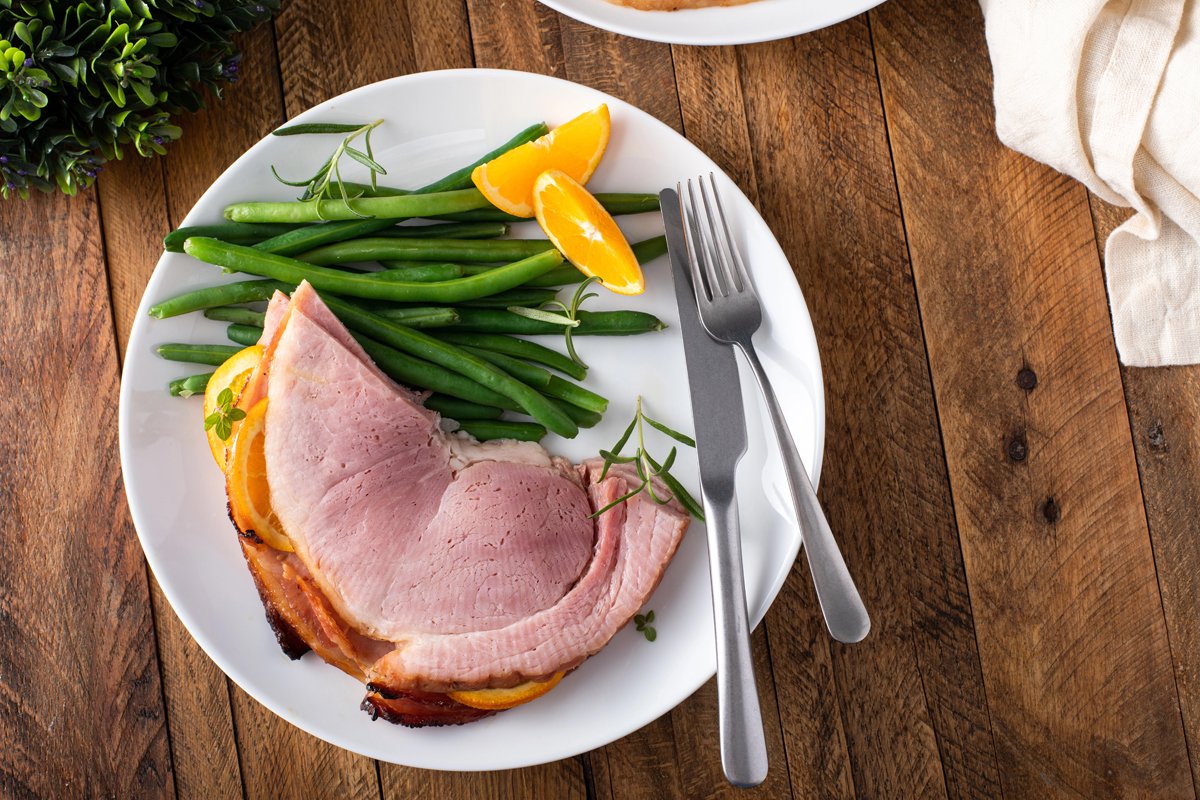 A serving of ham on a plate with some green beans.