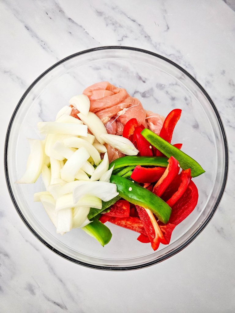 A bowl of thinly sliced peppers, onions, and chicken breast.