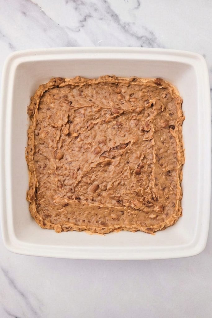 Refried beans spread in an even layer in a shallow baking dish.