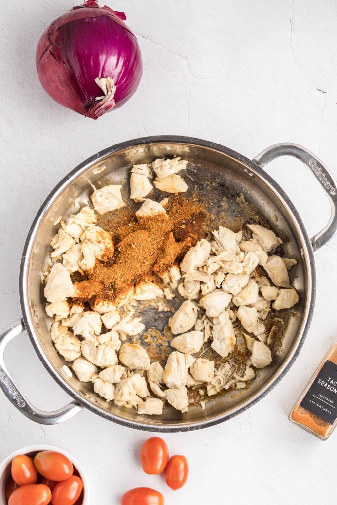 Chicken chunks and seasoning in a skillet.