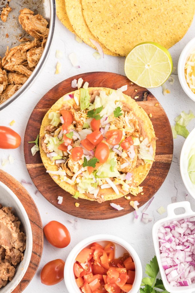 A chicken tostada on a round wooden cutting board.