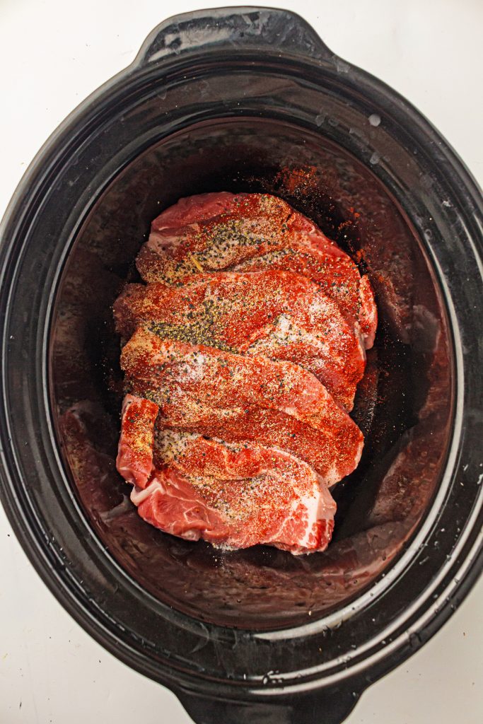 Pork steaks in a crockpot with seasoning on top.