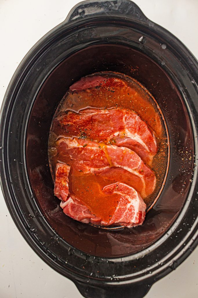 Seasoned pork steaks in broth in a crockpot.
