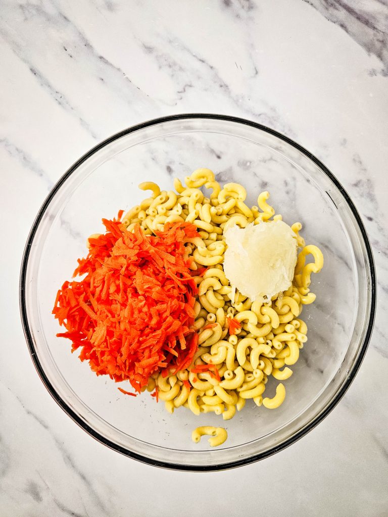 pasta, shredded carrots, shredded onions in a glass bowl