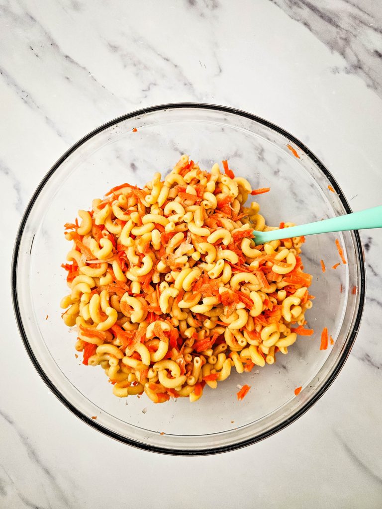 elbow macaroni mixed with shredded carrots and onions in a glass bowl