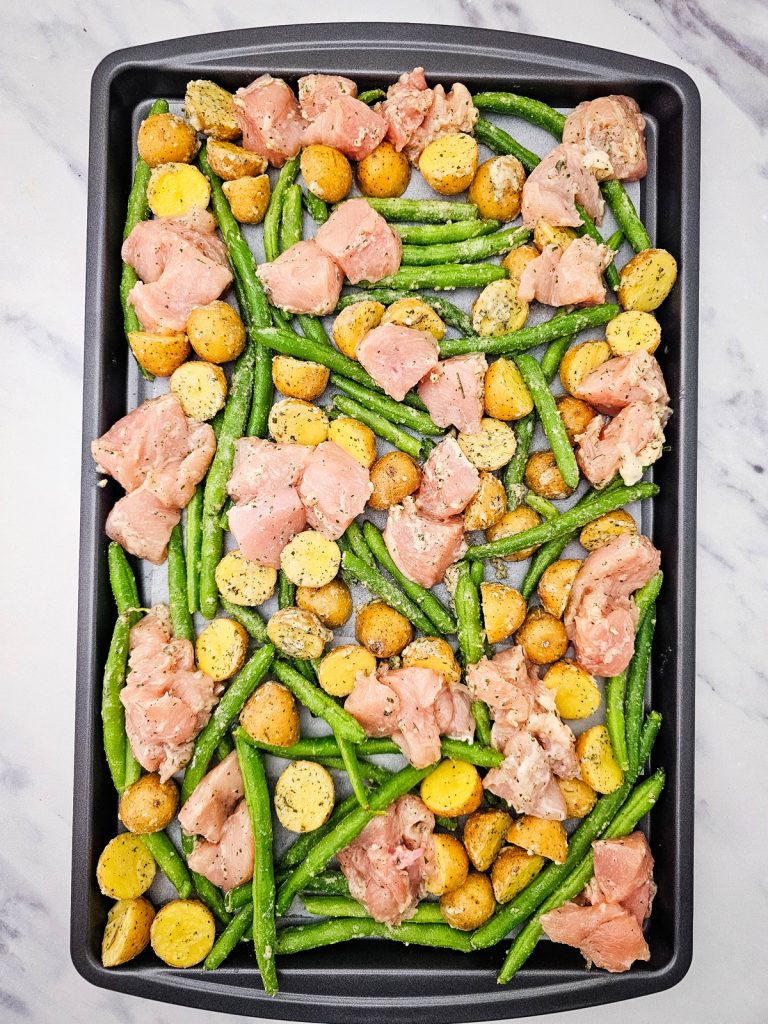 Seasoned chicken, potatoes and green beans spread on a sheet pan.