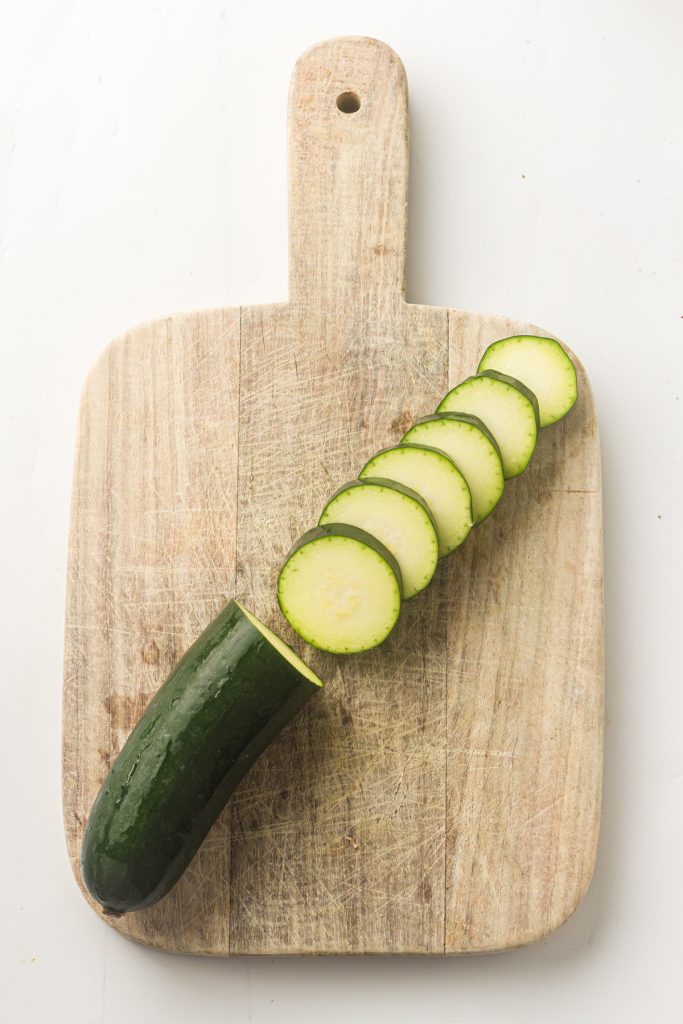 Sliced zucchini on a wooden cutting board.
