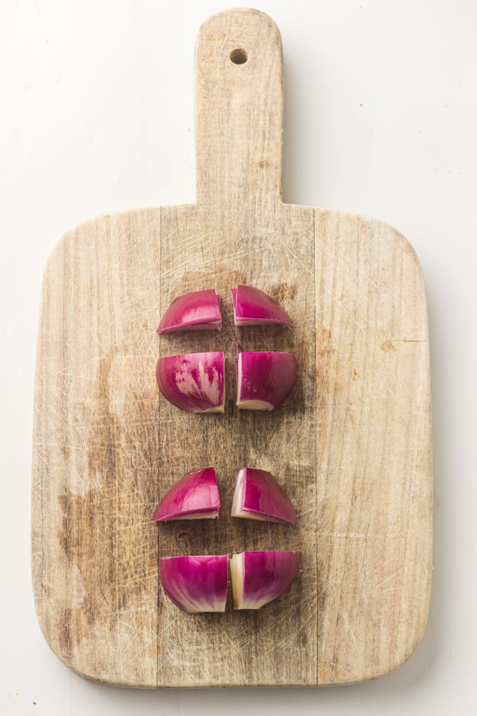 Red onion cut into quarters on a wooden cutting board.