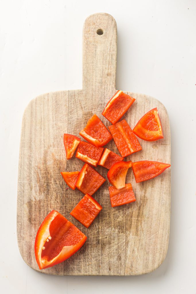 Red bell pepper cut into 1-inch pieces on a wooden cutting board.