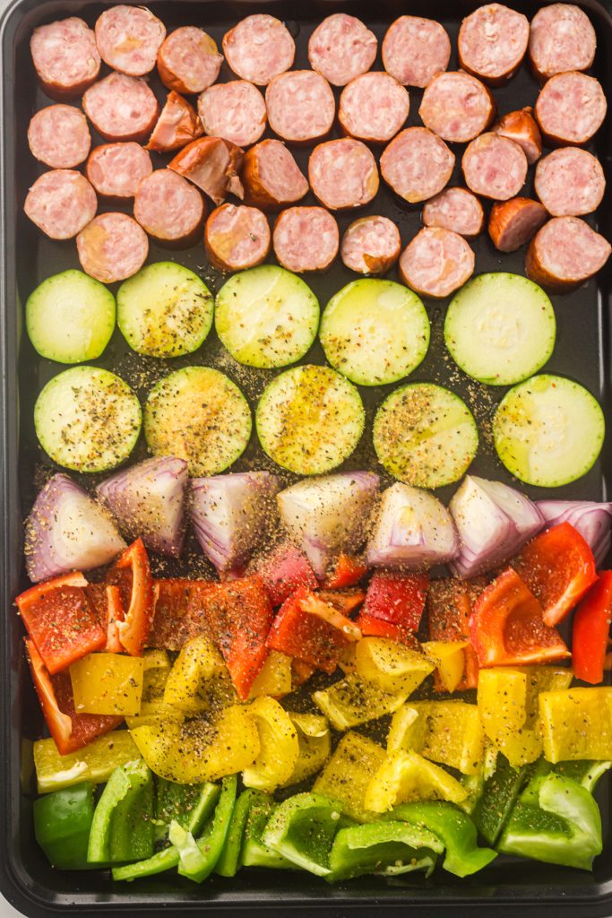 Sausage and vegetables on a sheet pan. The vegetables are seasoned.