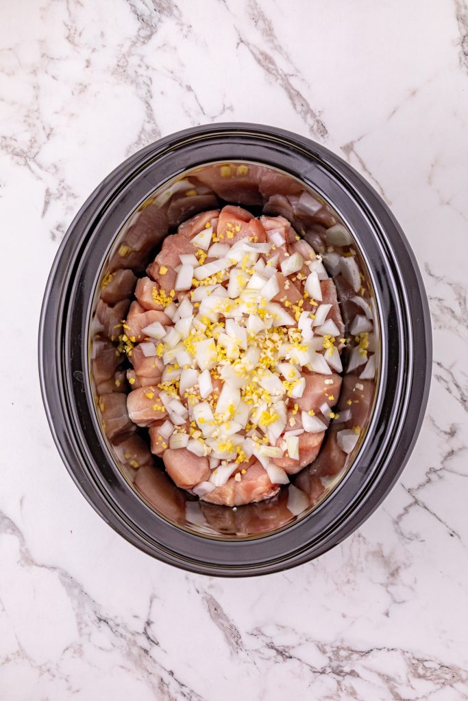Chopped chicken, diced onions, and minced garlic in a crockpot.