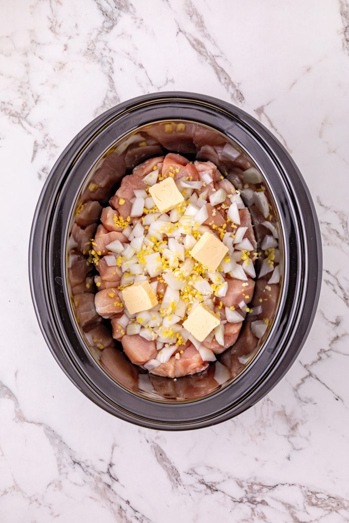 Chopped chicken, diced onions, and minced garlic with butter in a crockpot.