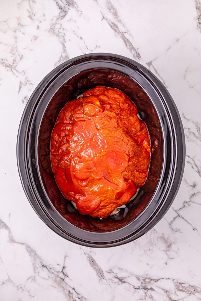 Seasoned tomato sauce poured over chicken pieces in a crockpot.