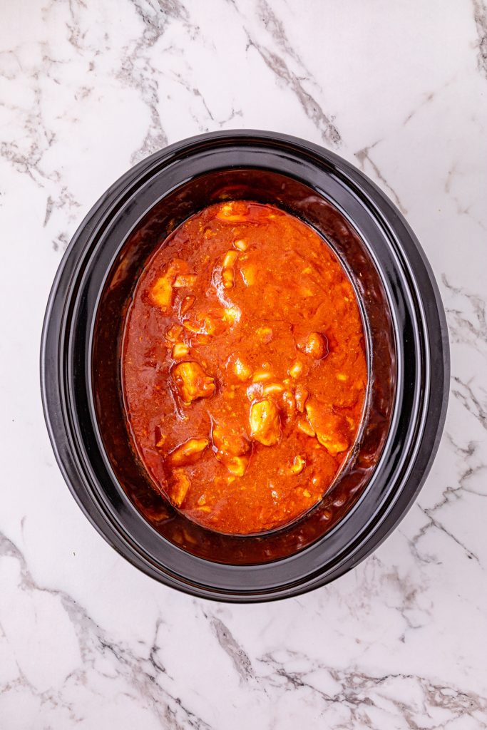 Seasoned tomato sauce poured over chicken pieces in a crockpot.