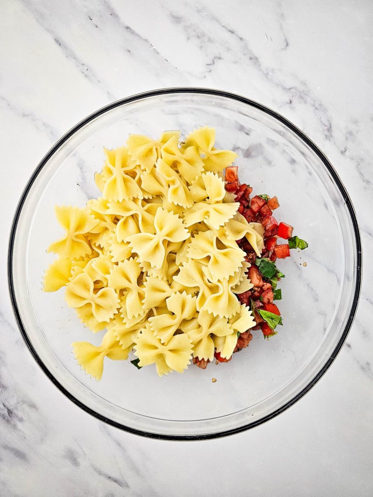 Bowtie pasta in a glass bowl with chopped tomatoes.