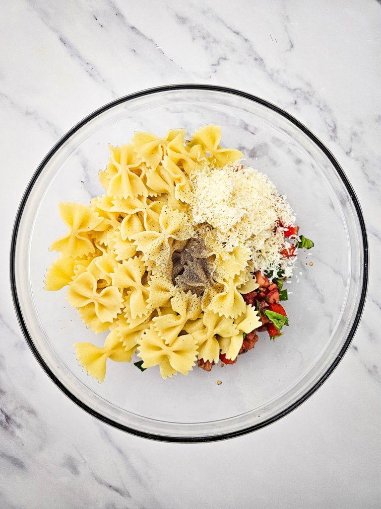Bruschetta pasta salad ingredients in a glass bowl.