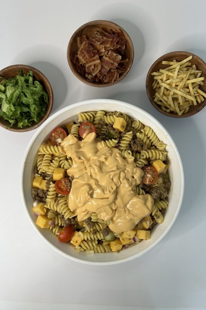 Pasta salad ingredients in a bowl topped with sauce.