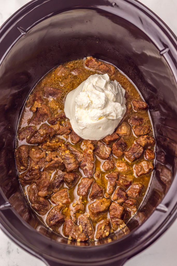 Sour cream added to beef chunks in a crockpot.