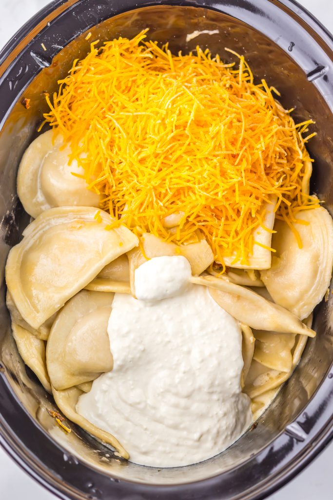 Pierogies, shredded cheese, and a creamy sauce in a crockpot.